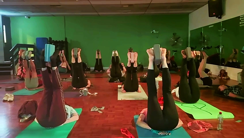 A full class lying on their mats with legs raised, using yoga blocks