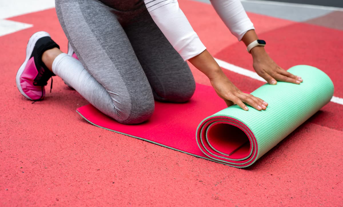 Someone kneeling to unroll a yoga mat